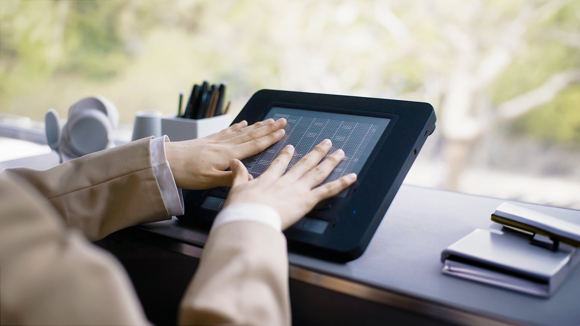The Dot Pad placed on a desk with two hands exploring a tactile graphic of a chart