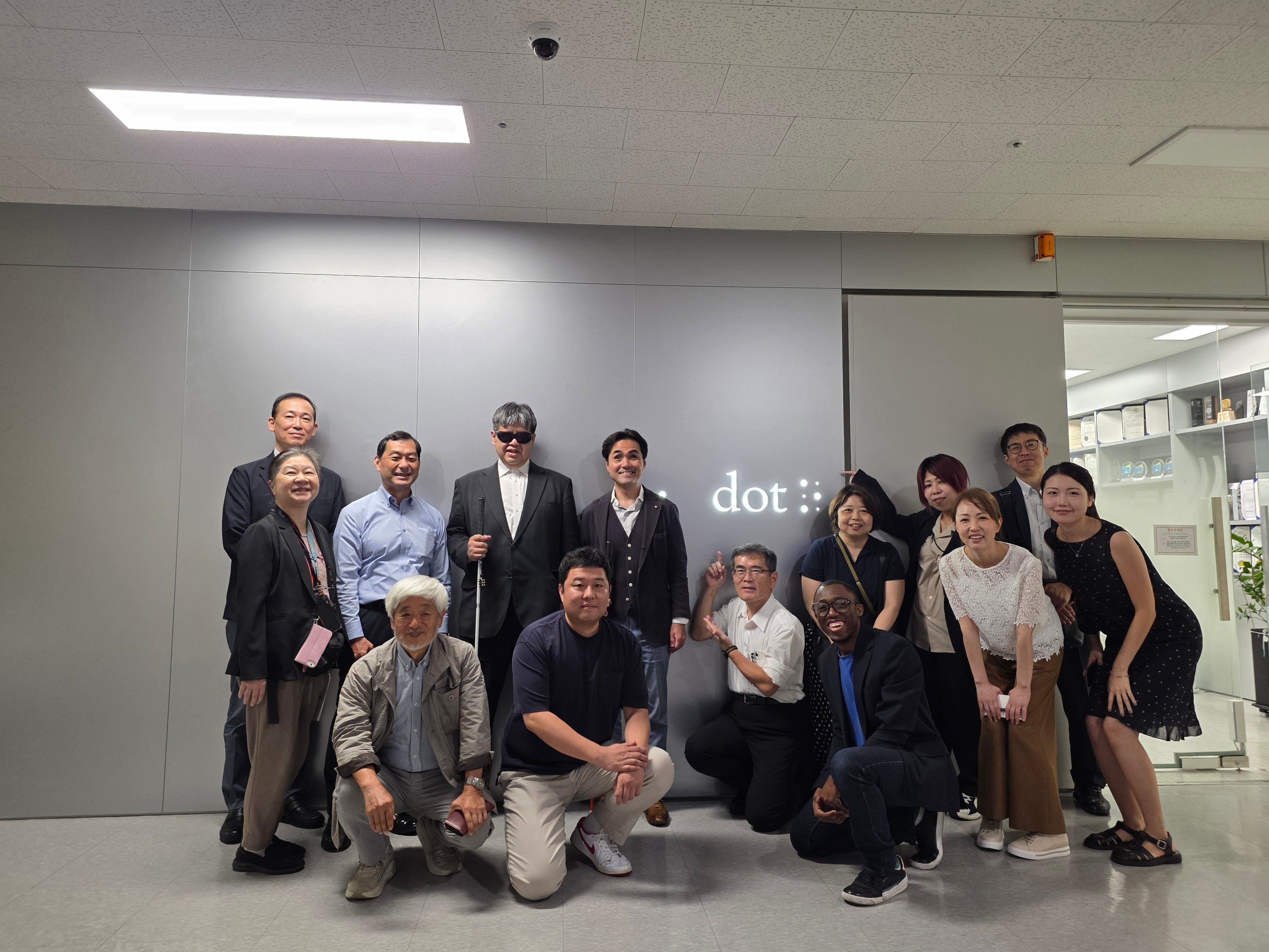 Dot staff and the Japanese delegation stand and kneel in a large group infront of the Dot Inc. logo at the Dot office in Seoul