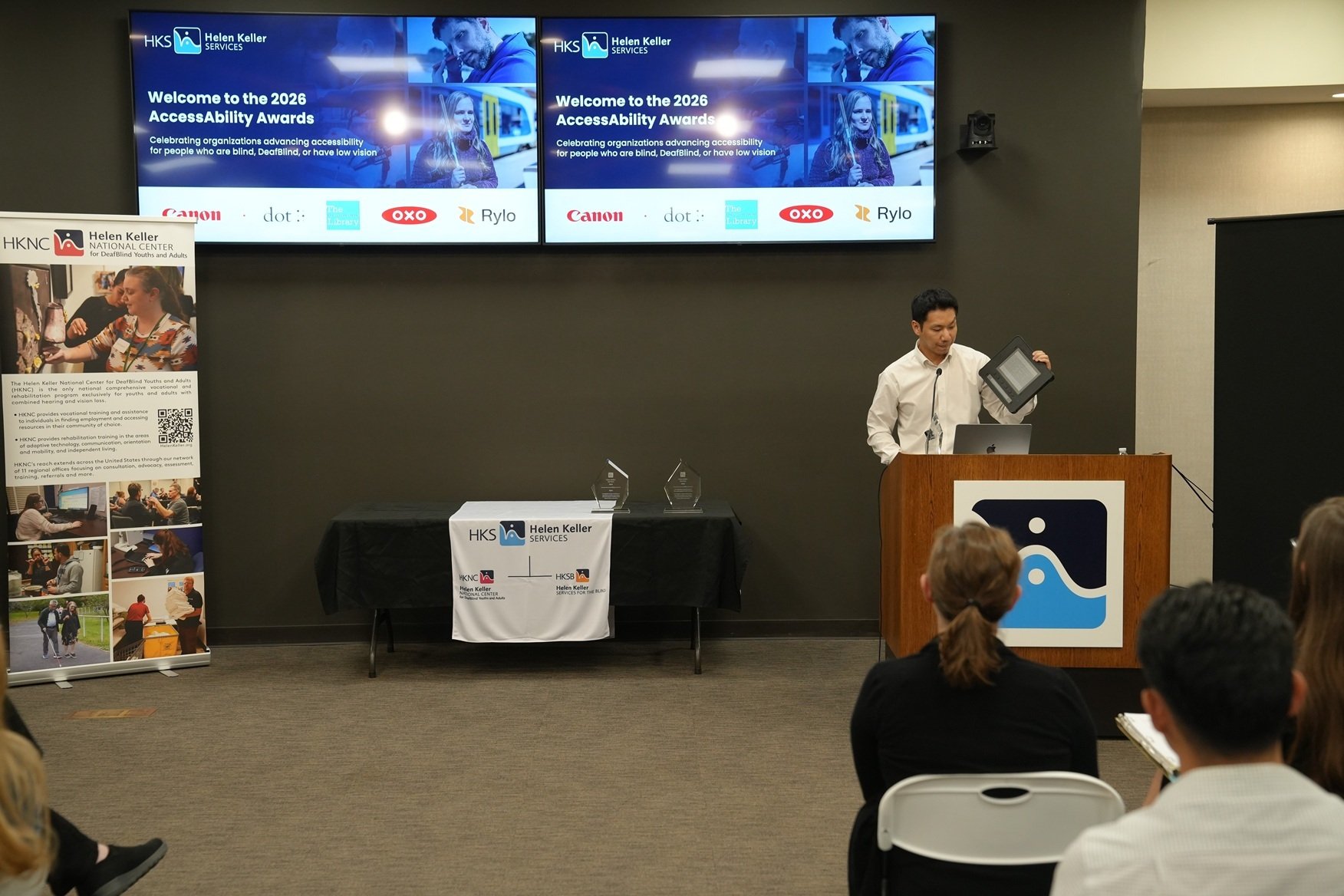 Ki from Dot Inc accepting the award. Ki stands at the front of the room holding a Dot Pad X up to demonstrate its functionality.