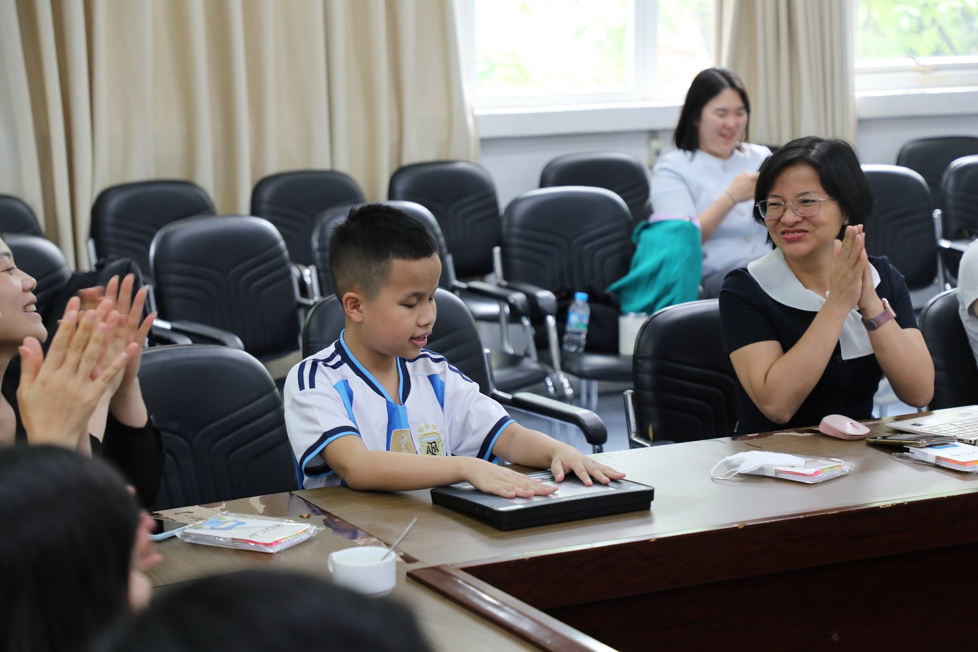 Young boy wearing football shirt using a Dot Pad while two ladies on either side clap and smile warmly